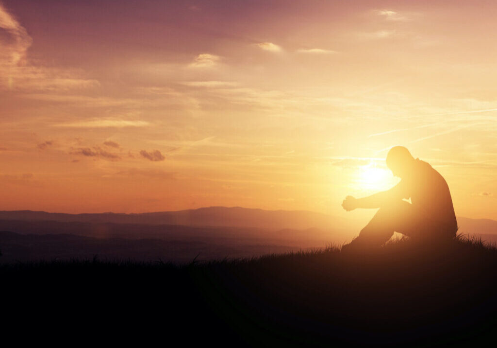 Man praying as the sun rises in the mountains.